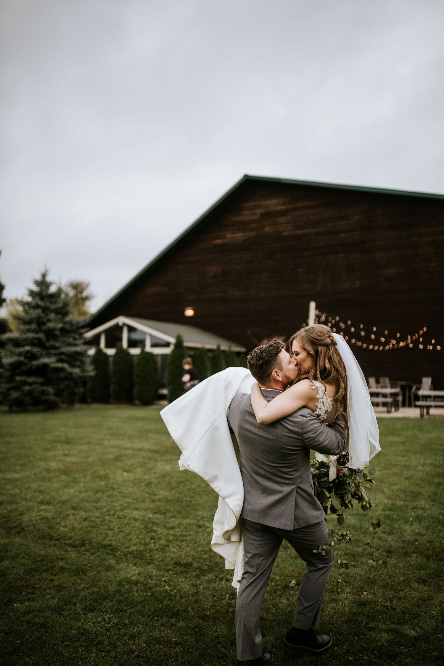 Wedding couple sharing romantic kisses against a rustic barn backdrop with string lights.