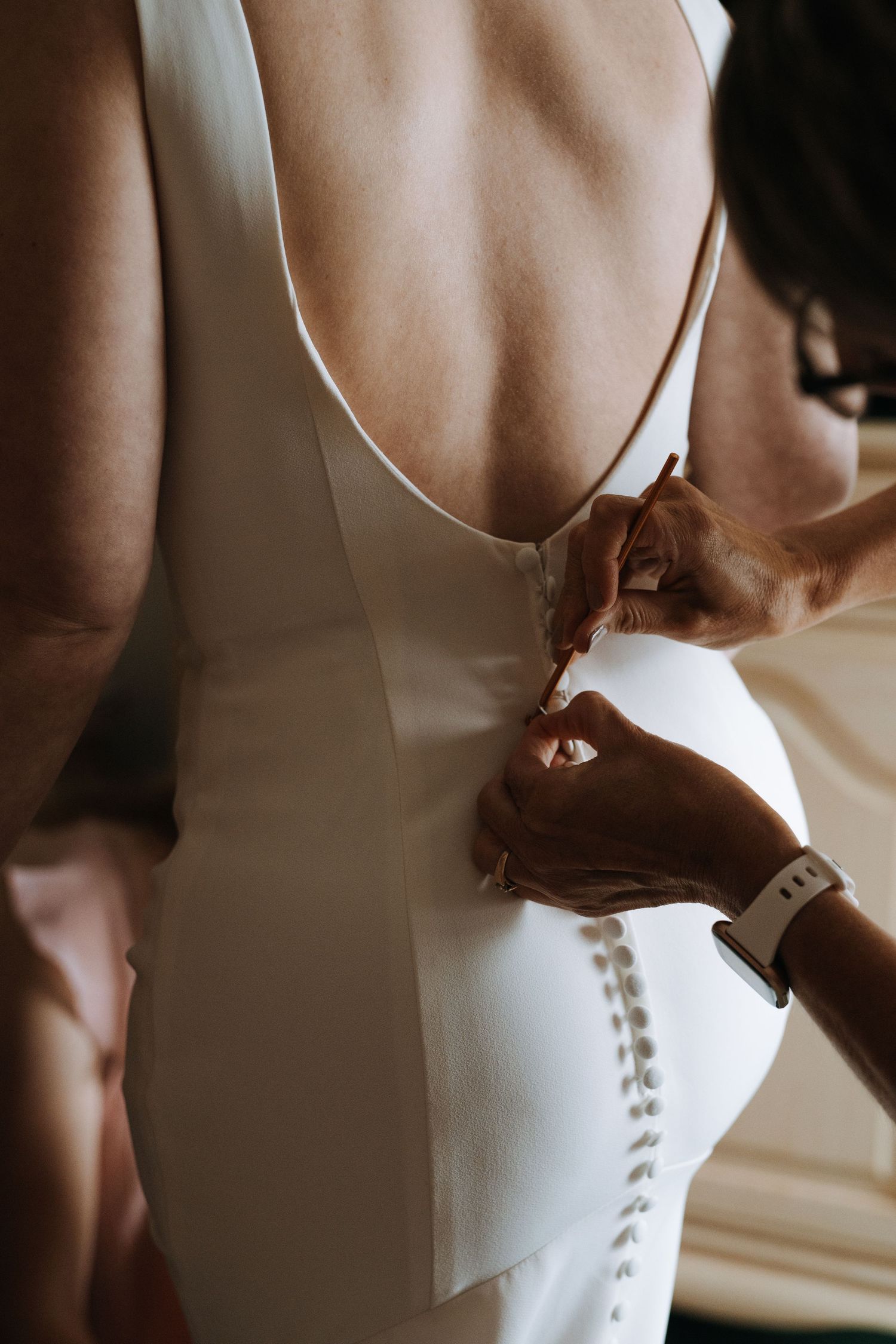 Close-up details of buttoning up a classic white wedding dress with pearl buttons.
