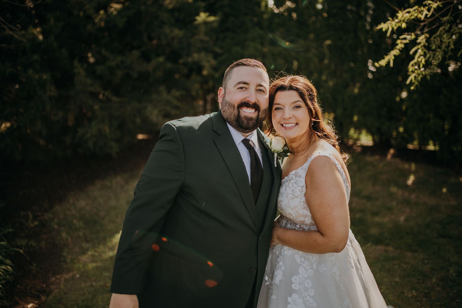 A joyful wedding portrait captured in golden sunlight against evergreen trees.