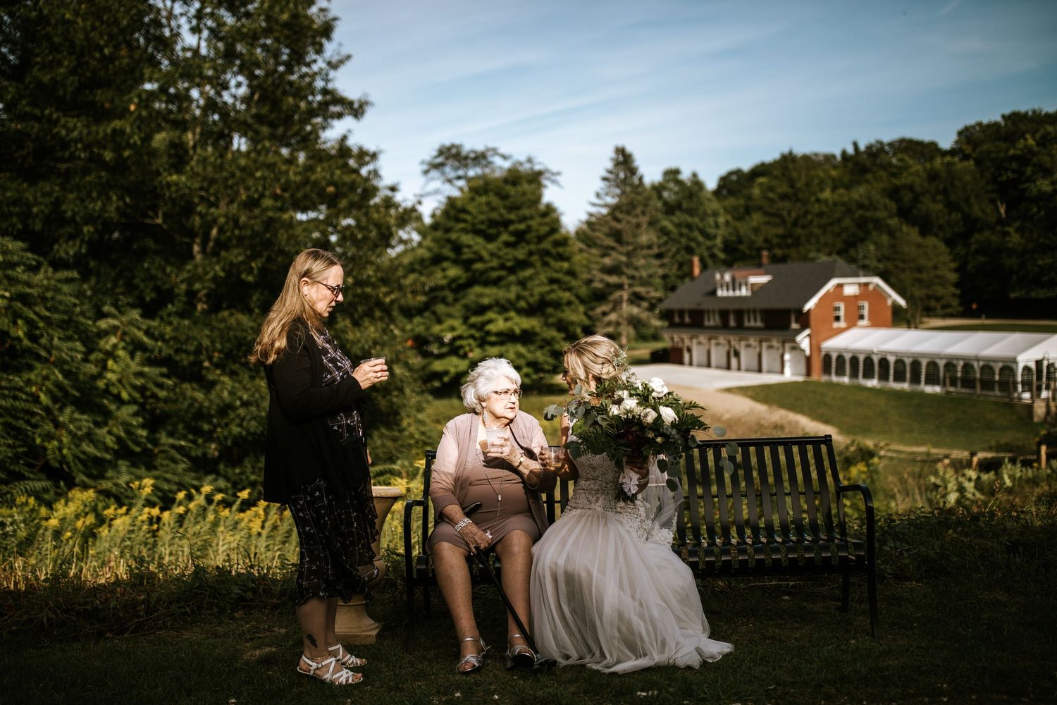 Outdoor wedding reception under blue sky with garden and trees in background.