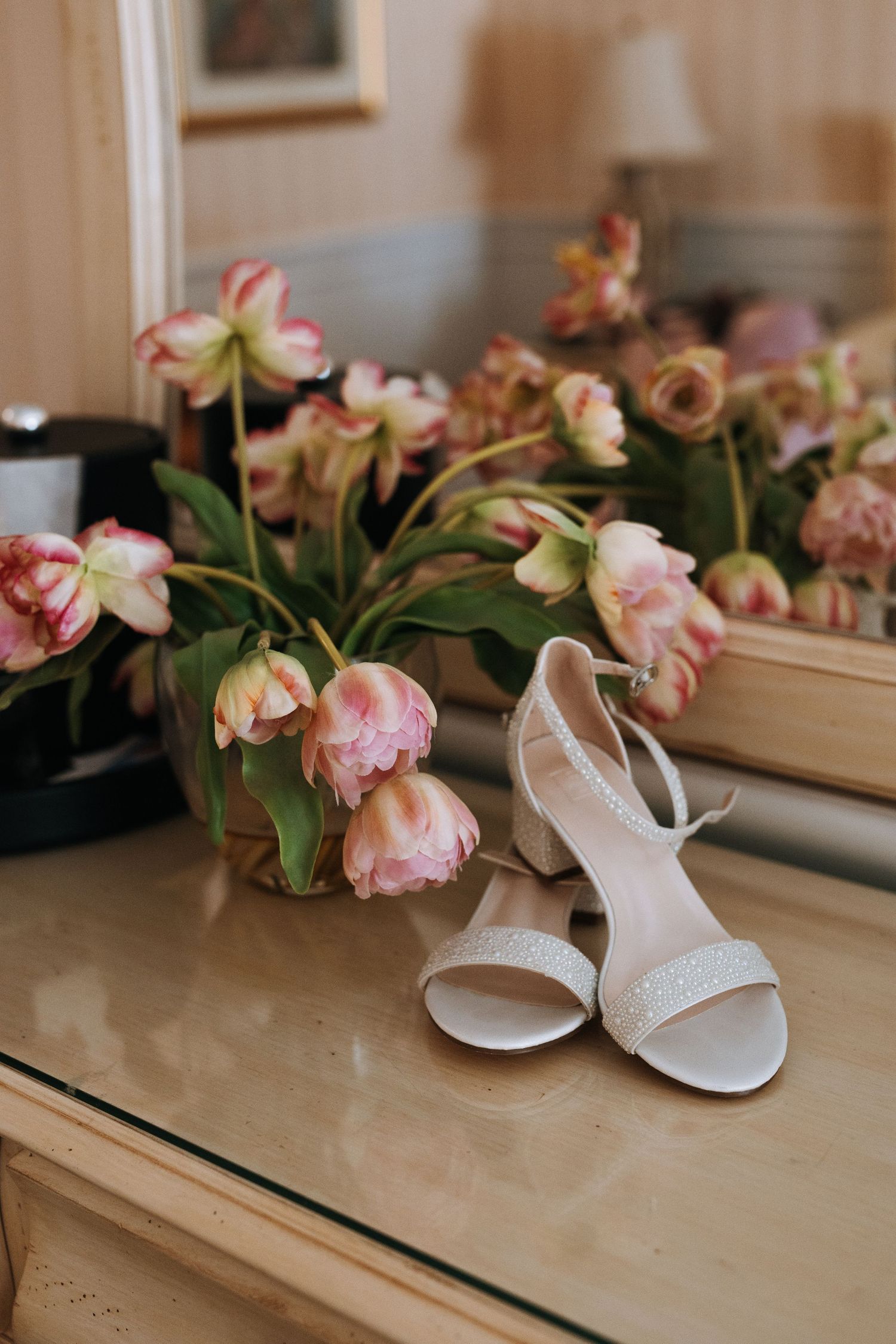 White bridal sandals next to pink tulips on wooden dresser.