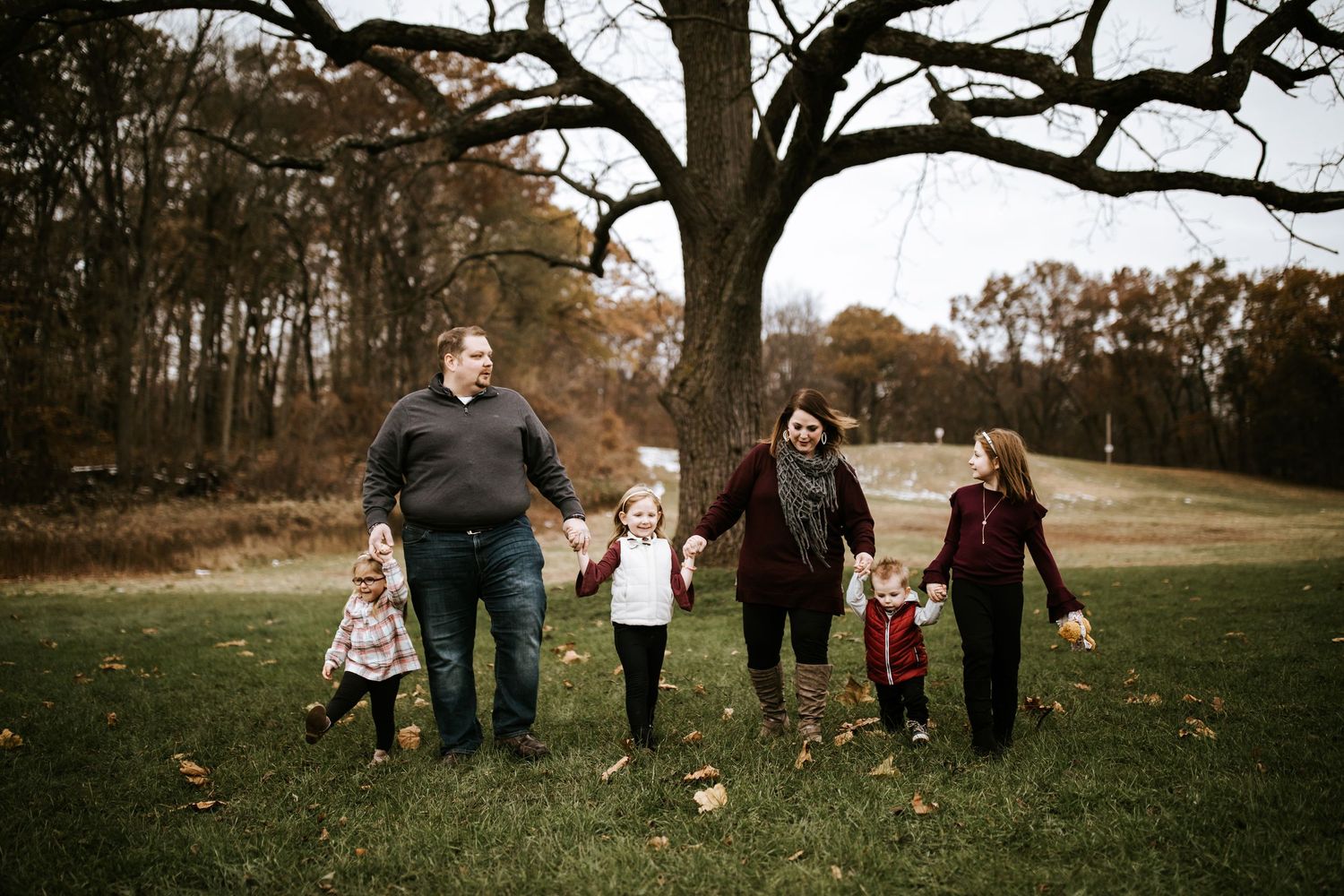 Family photo session under large tree branches during autumn season.