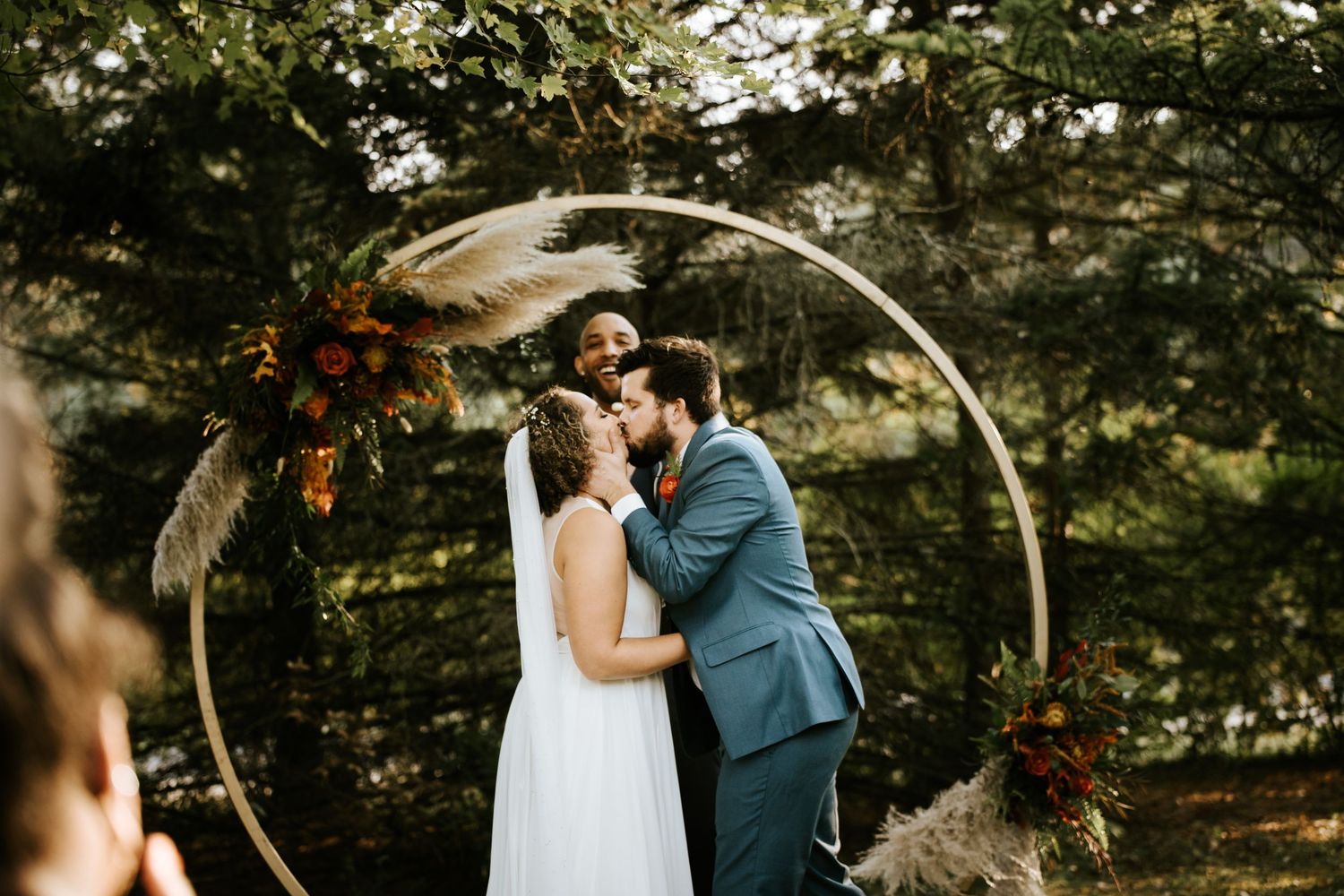 Outdoor wedding ceremony setup with white arch and natural forest backdrop.