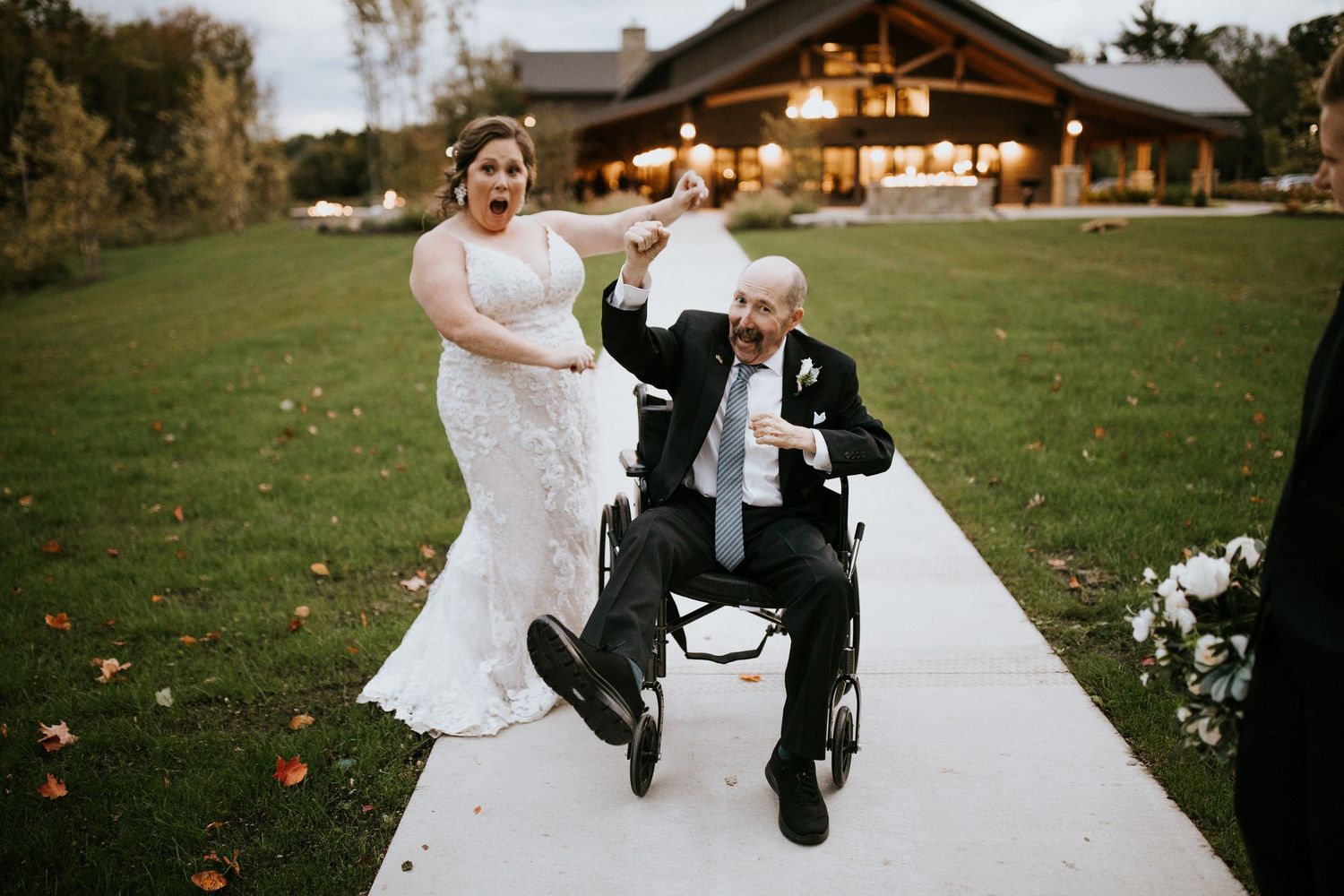A heartwarming outdoor wedding scene with a bride and wheelchair user celebrating together on a path near a rustic lodge.