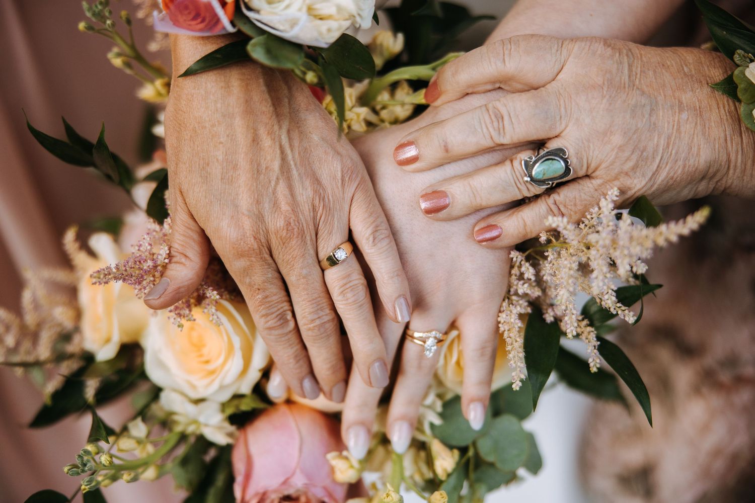Multiple generations display their rings over a bouquet of pink and cream roses.