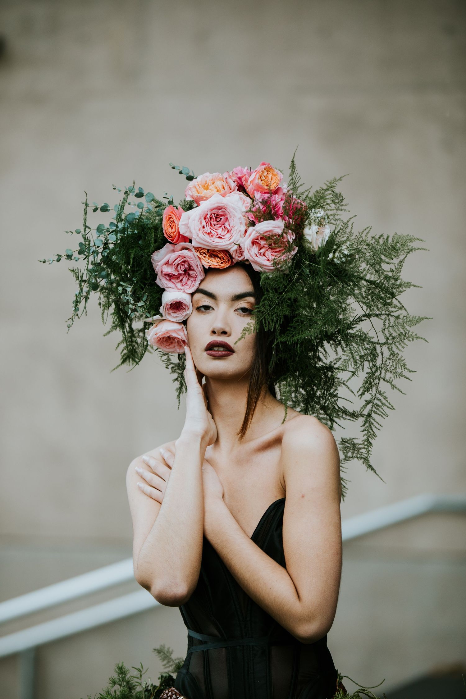 Artistic portrait wearing floral crown with pink roses and greenery against grey background.