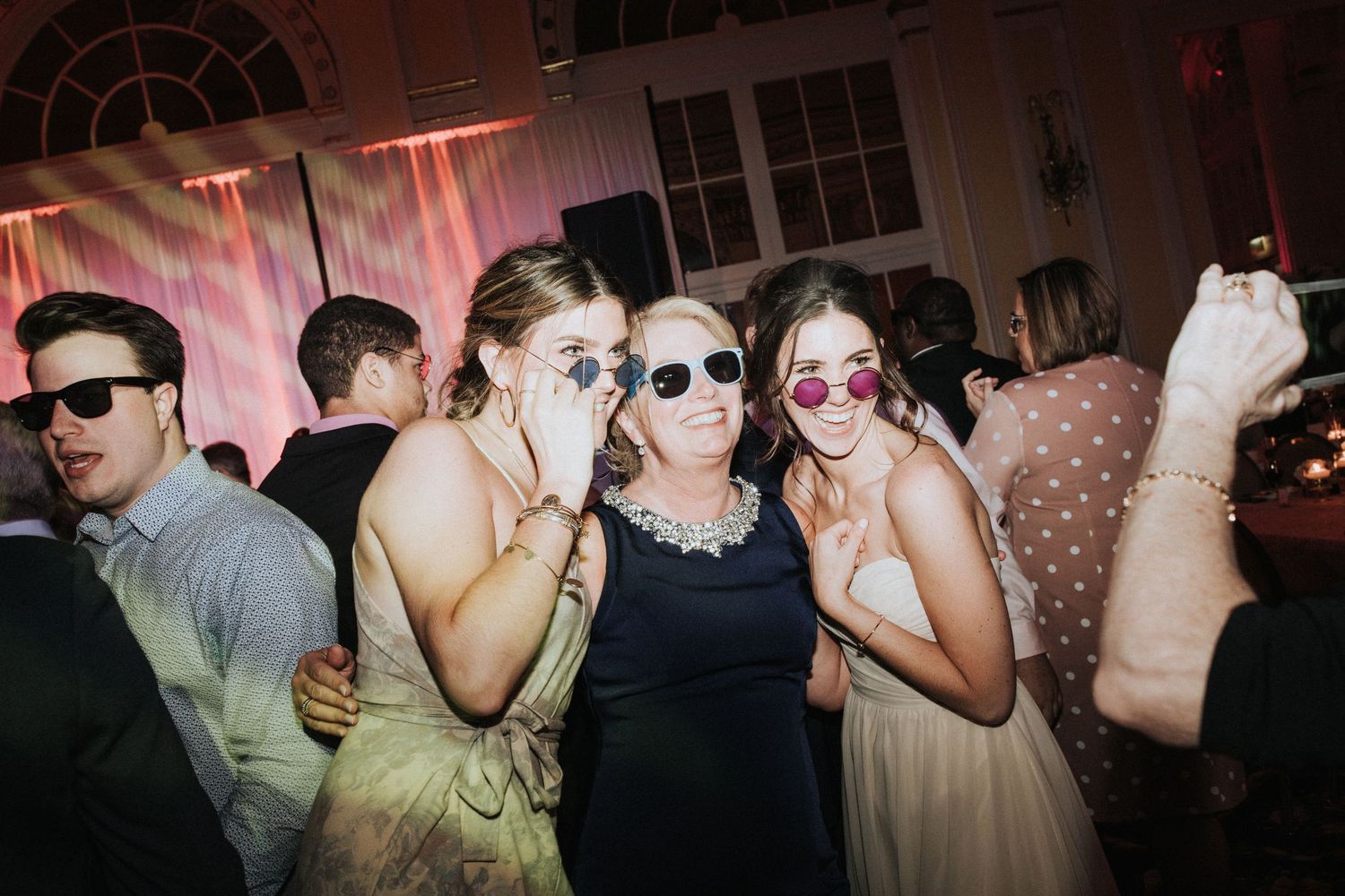 Wedding guests dancing and celebrating at a reception with pink lighting effects.
