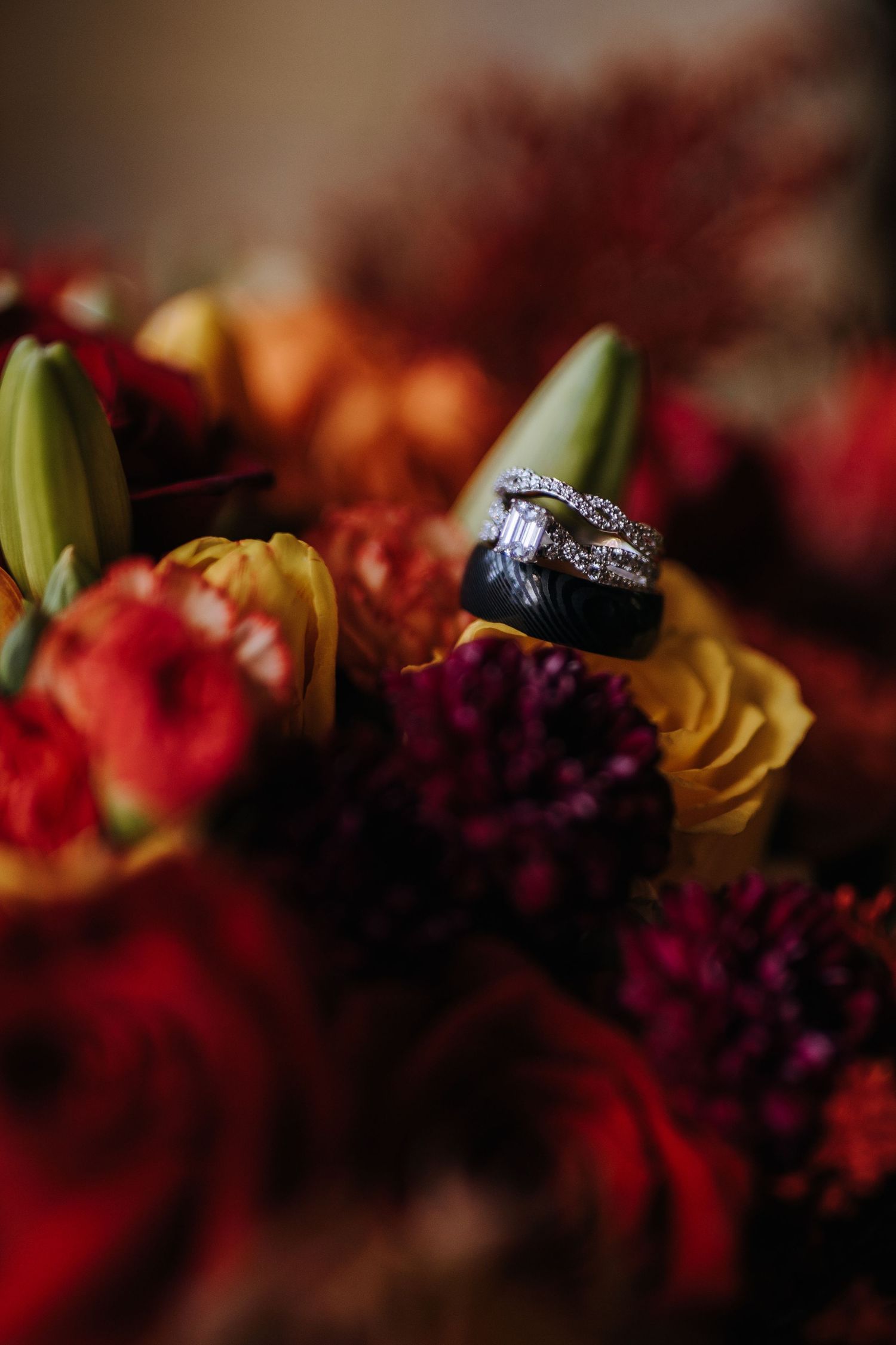 Wedding rings displayed on vibrant autumn-colored flowers with lilies and roses.