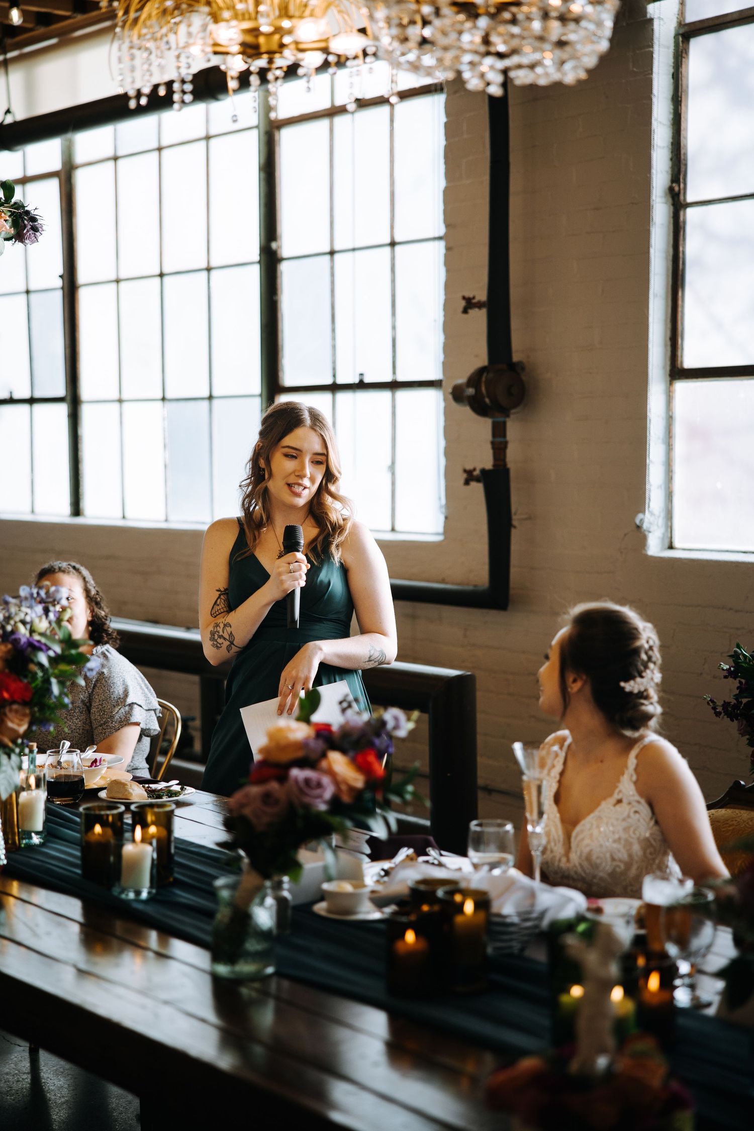 Reception celebration with chandelier lighting and industrial windows.