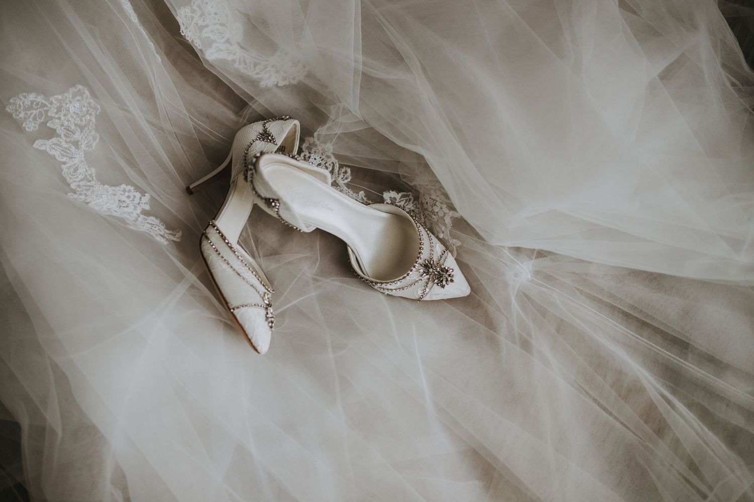 A delicate white wedding dress with lace details and tulle fabric laid out on display.