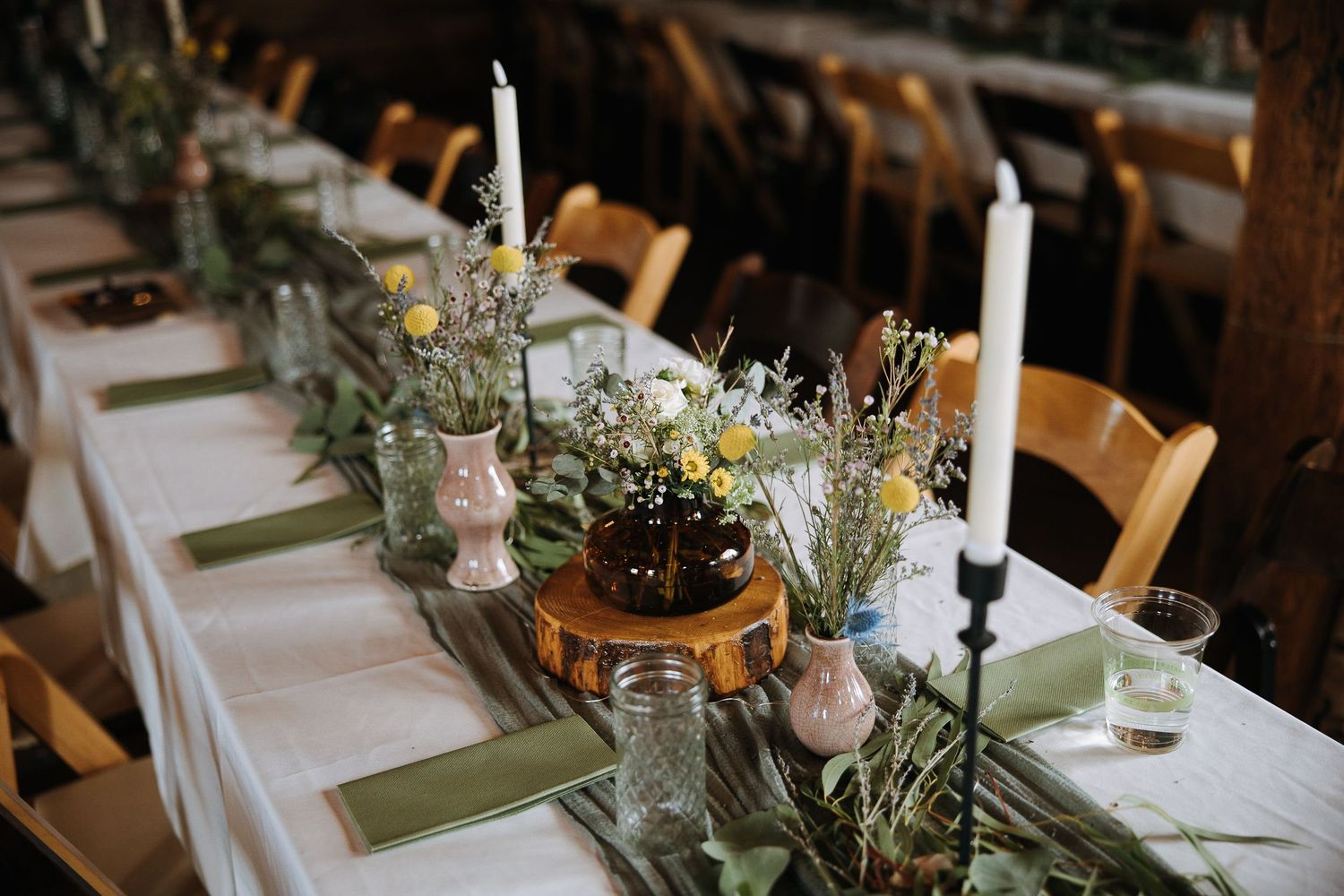 Elegant wedding reception table settings with white linens, candles and sage green accents.