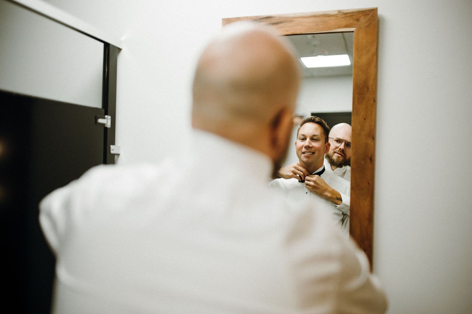 Reflection in a wooden-framed mirror shows preparations before a formal event.