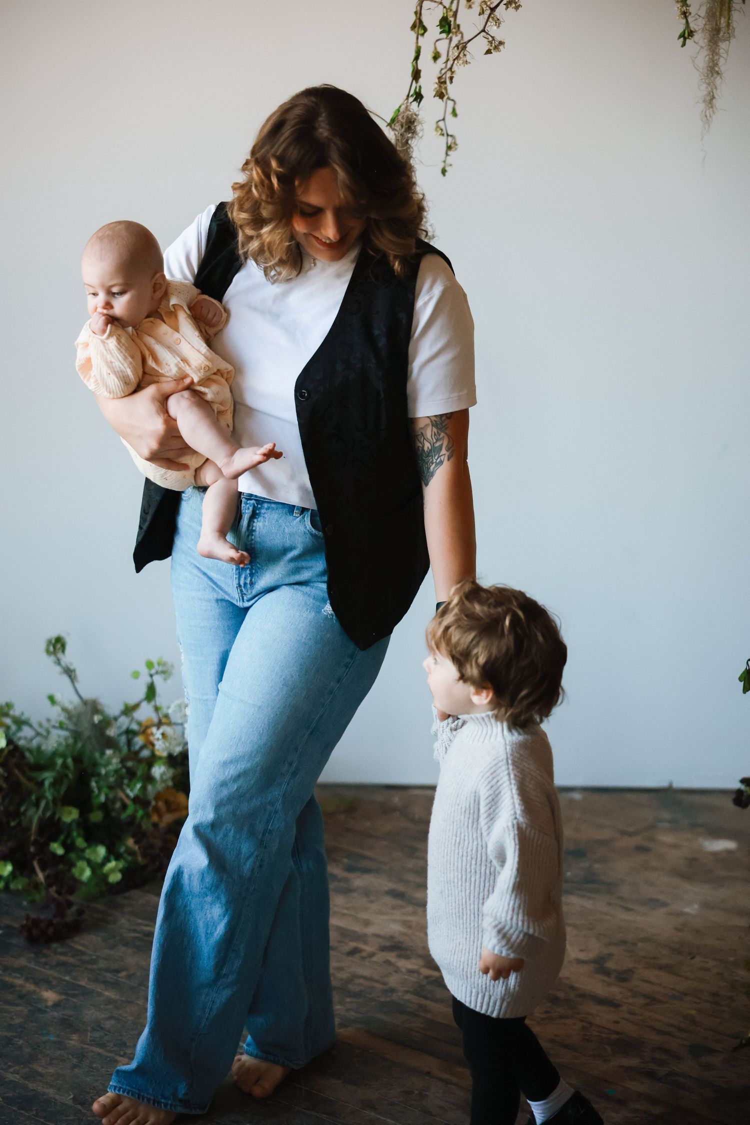 Casual family portrait with children in front of white wall with hanging plants.