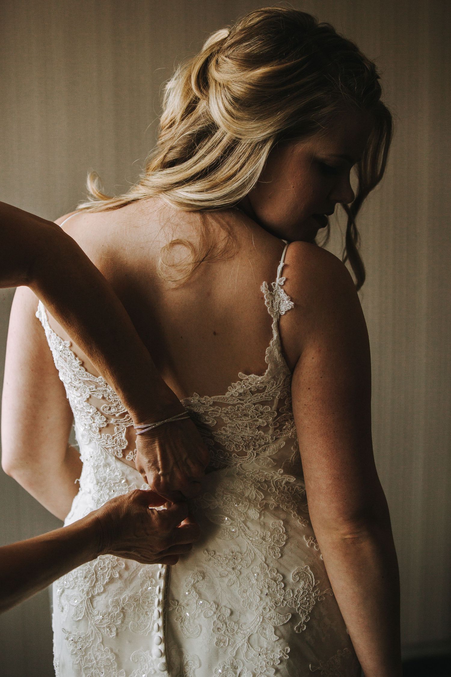 A series of photos showing the intricate details of a white lace wedding dress in moody lighting.