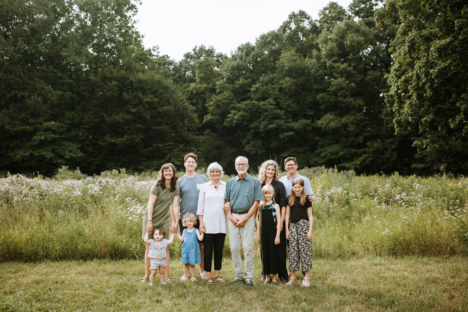 Family group gathered in a sunny meadow surrounded by trees and tall grass.