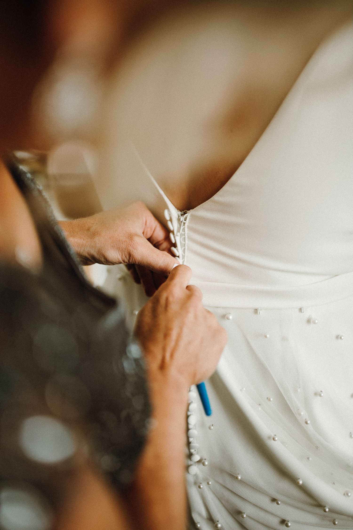Close-up shot of hands lacing up a white wedding dress with delicate details and pearls.