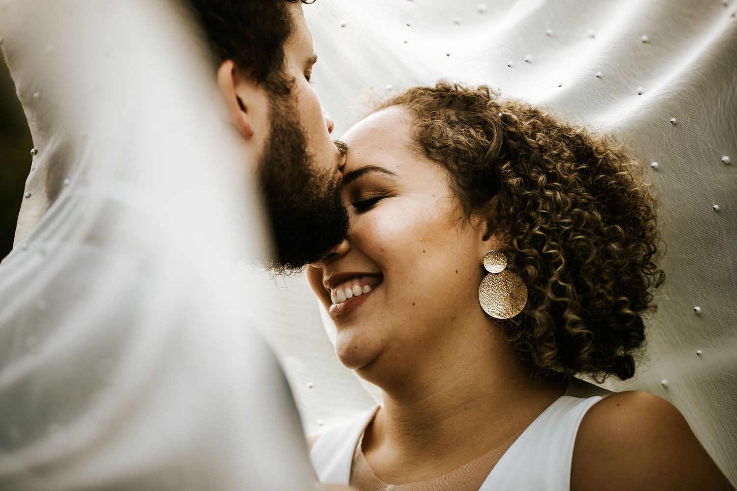 Close-up artistic wedding portrait with soft lighting and white veil details.