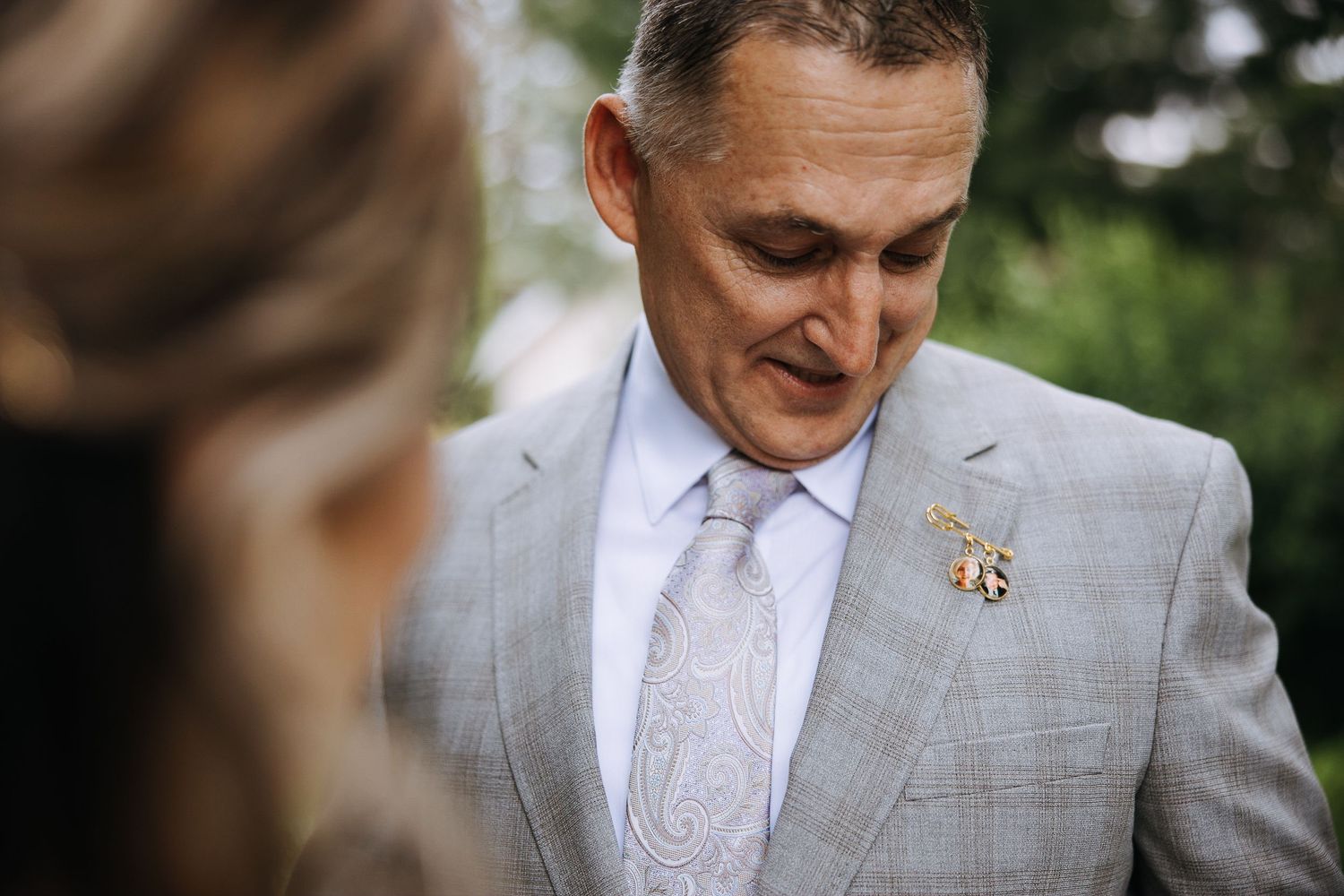 Groom in light gray suit smiling during outdoor wedding ceremony.