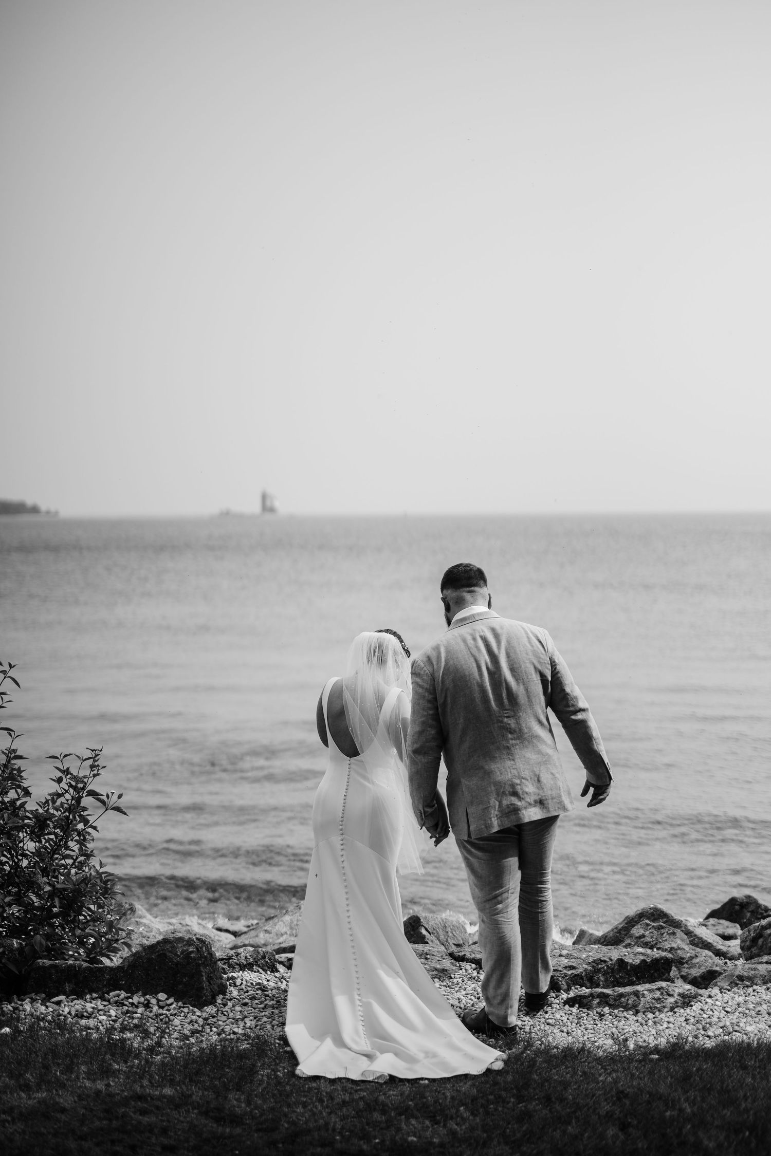 A black and white photo of a couple walking along a rocky shoreline.