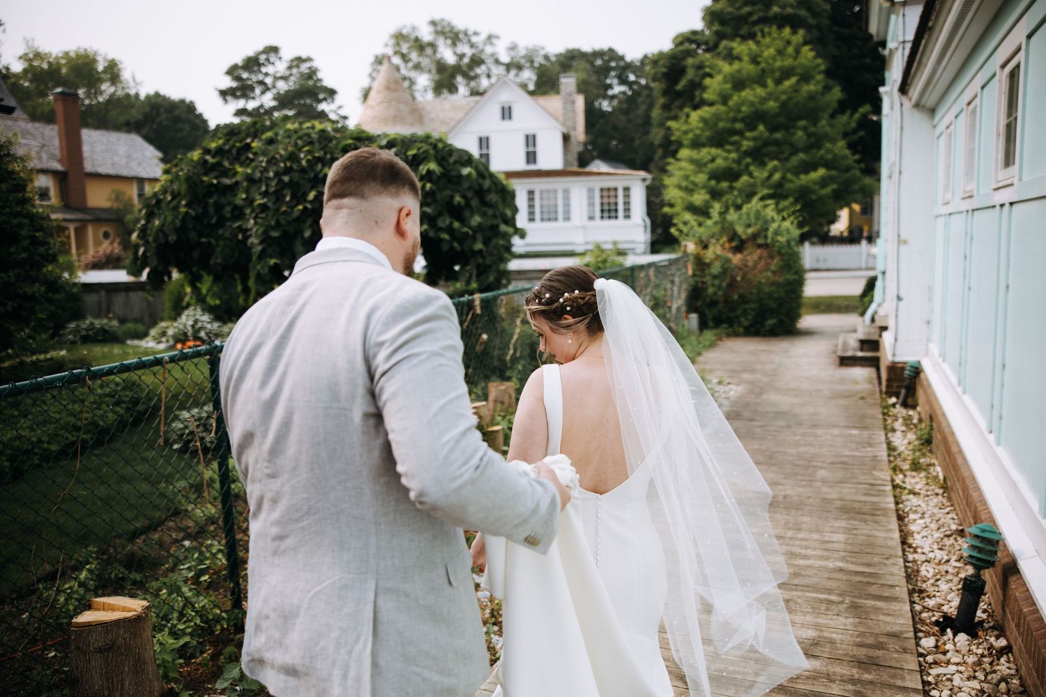 A wedding couple poses outside a charming coastal building with white siding.