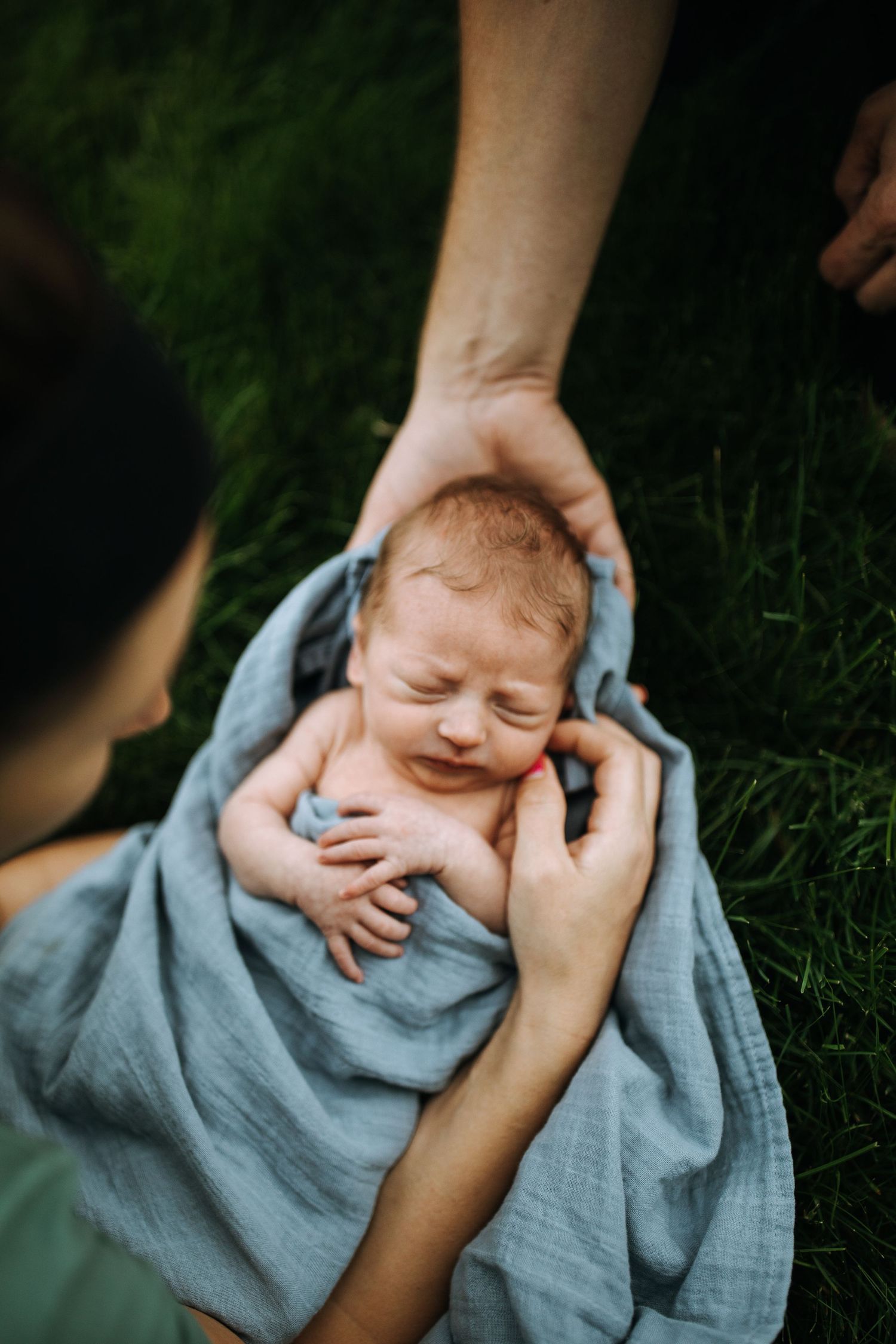 Baby wrapped in gray blanket lying on grass during an outdoor photoshoot.