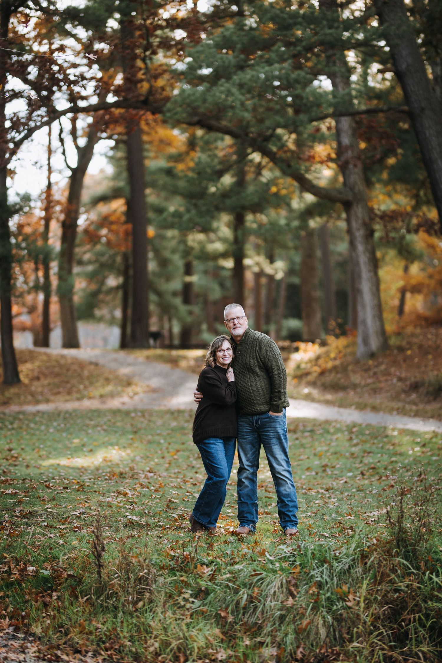 Two people stroll along a winding path through a wooded area during fall.