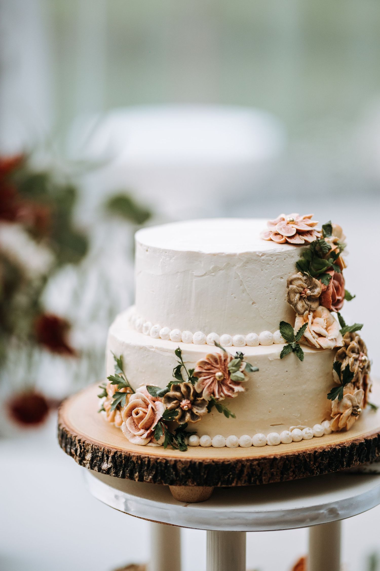 Simple white wedding cake decorated with copper flowers sits on wooden slice cake stand.