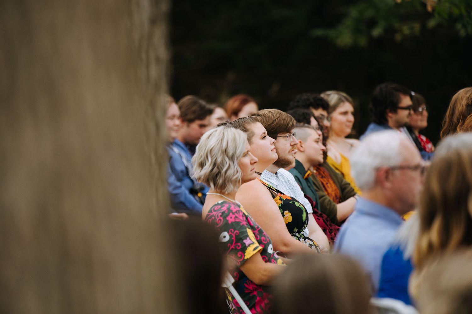 Wedding guests seated outdoors for a ceremony under trees.