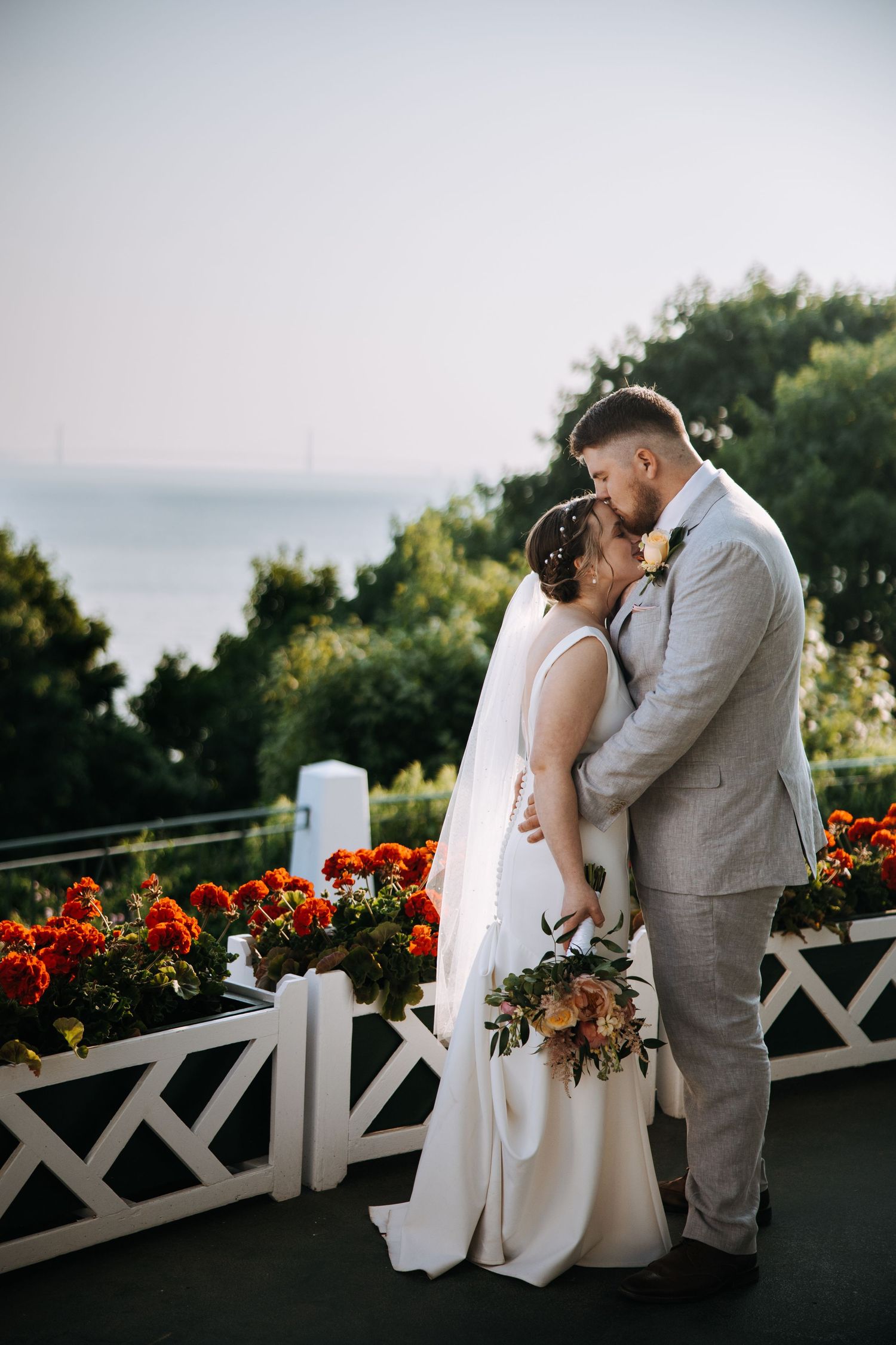 Couple shares intimate moment on balcony with red flowers and white railing at dusk.
