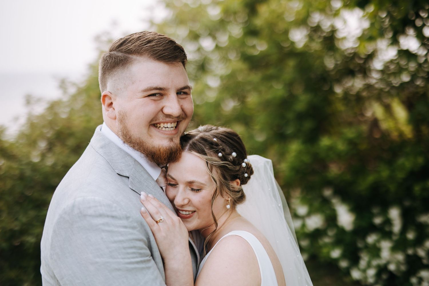 A romantic wedding couple shares an intimate moment outdoors surrounded by lush greenery.