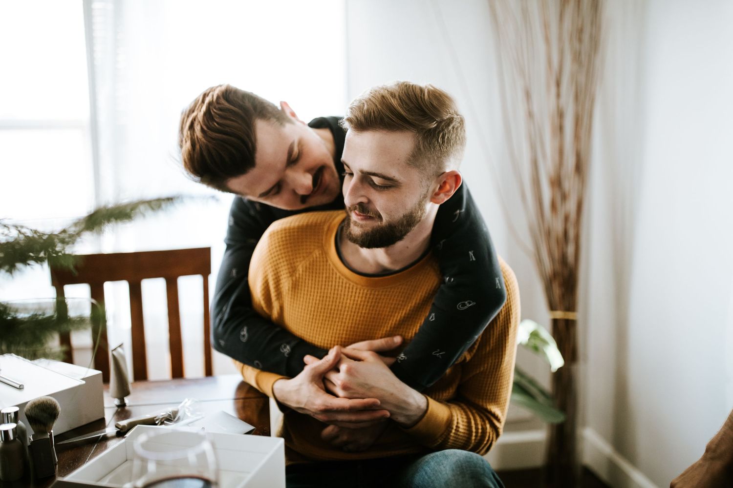 A couple shares an intimate moment while sitting together on a couch in a sunlit room.