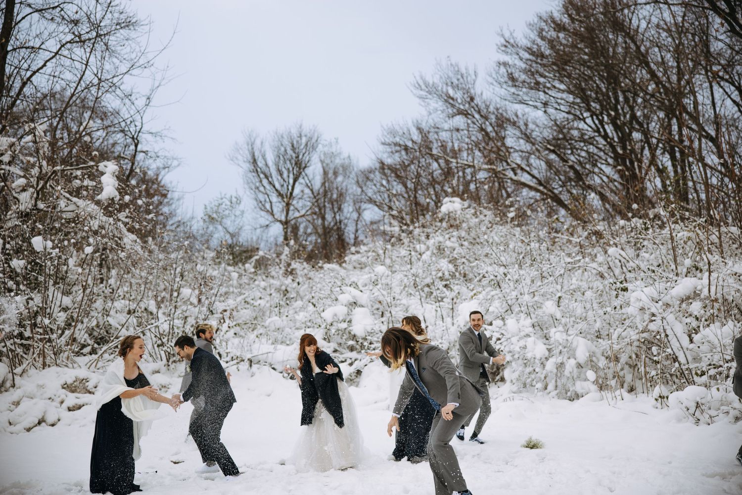 Wedding group having fun and throwing snow in a winter wonderland setting.
