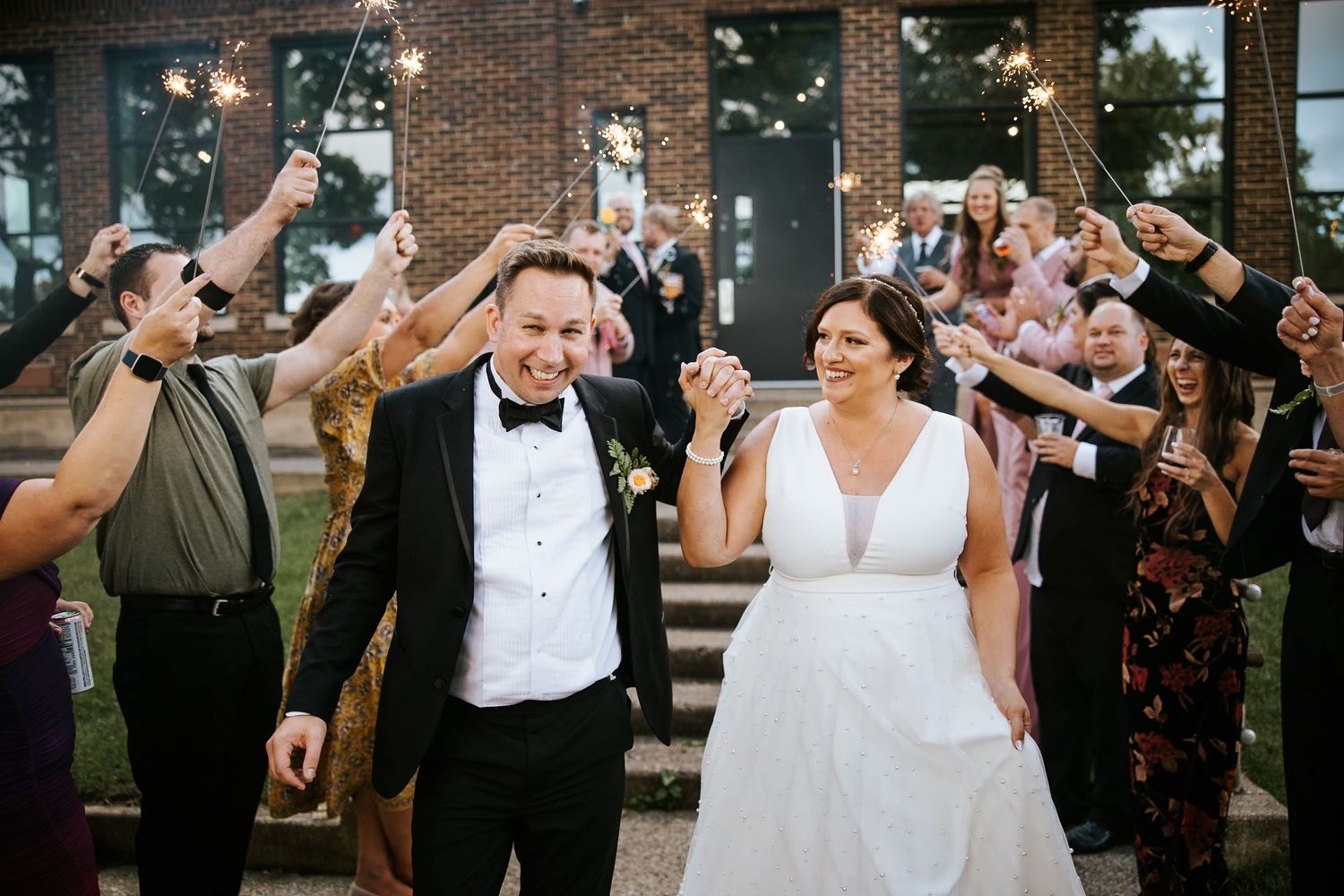 Wedding party celebrates with confetti toss outside brick venue.