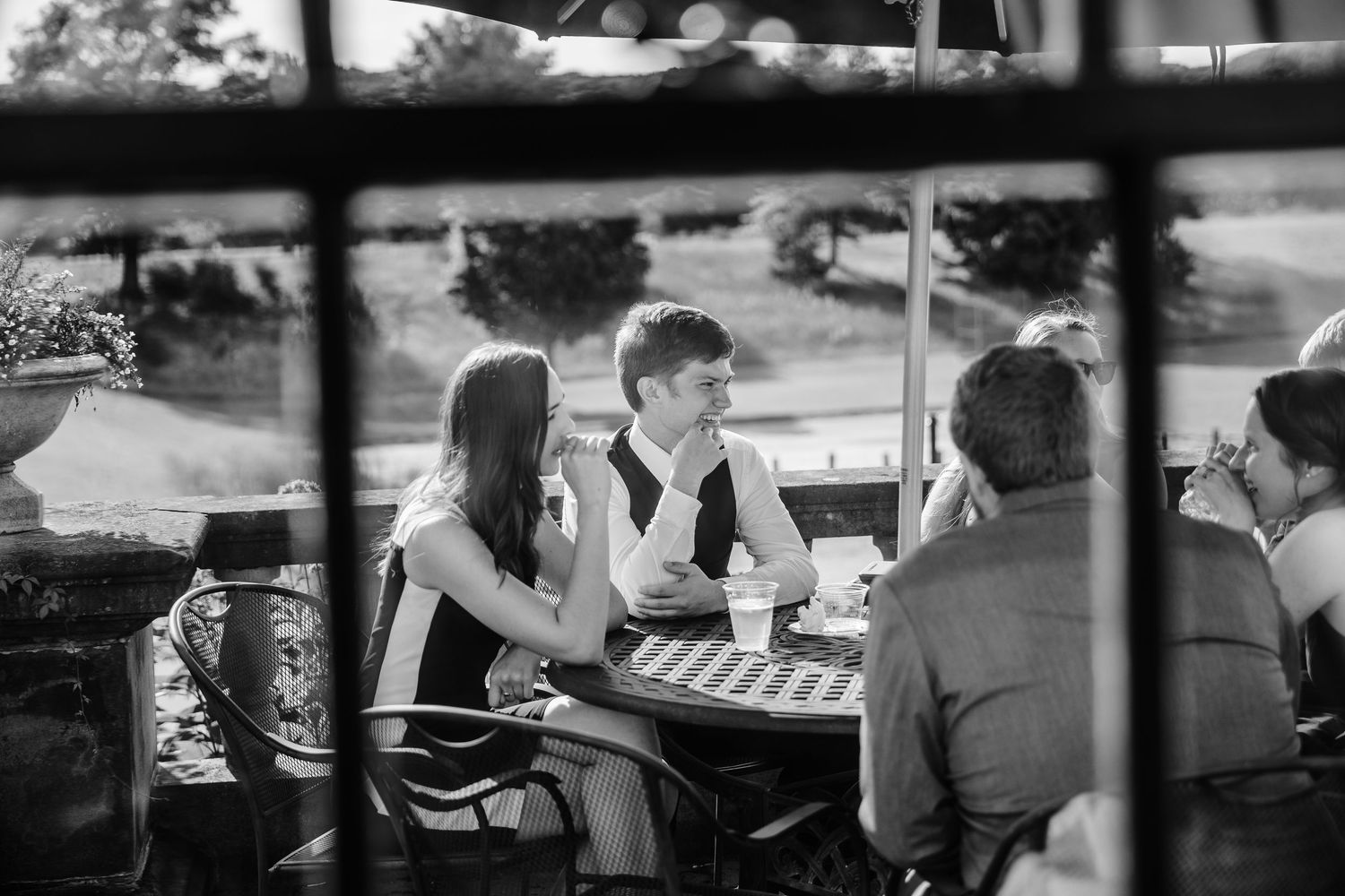 Wedding reception tables viewed through window panes with guests seated outdoors.