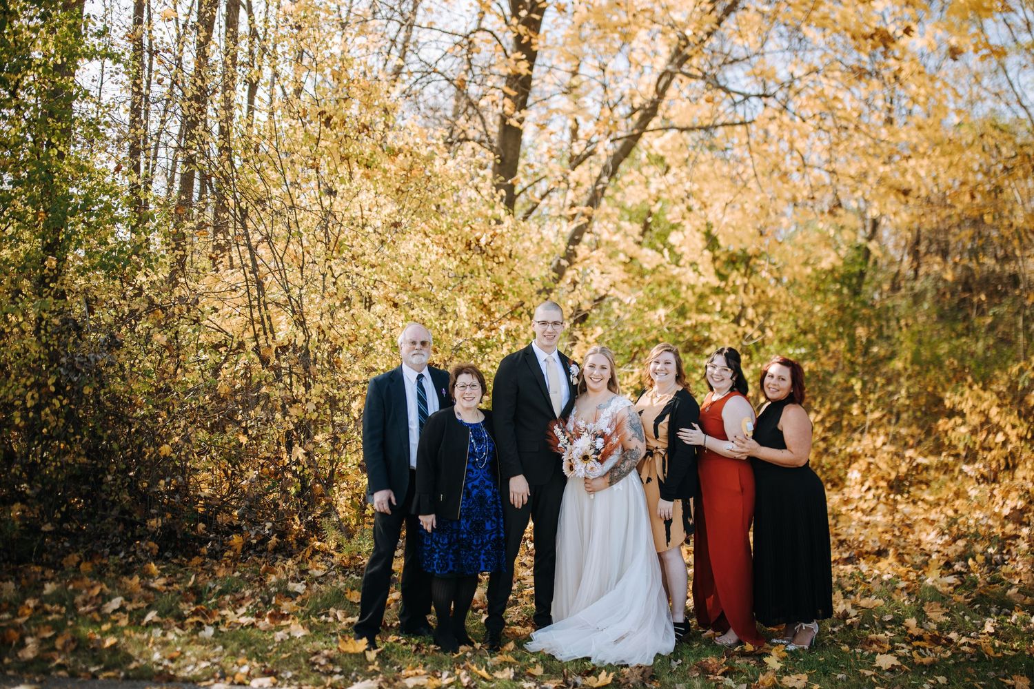 Wedding party poses for autumn portraits among golden-leaved trees.