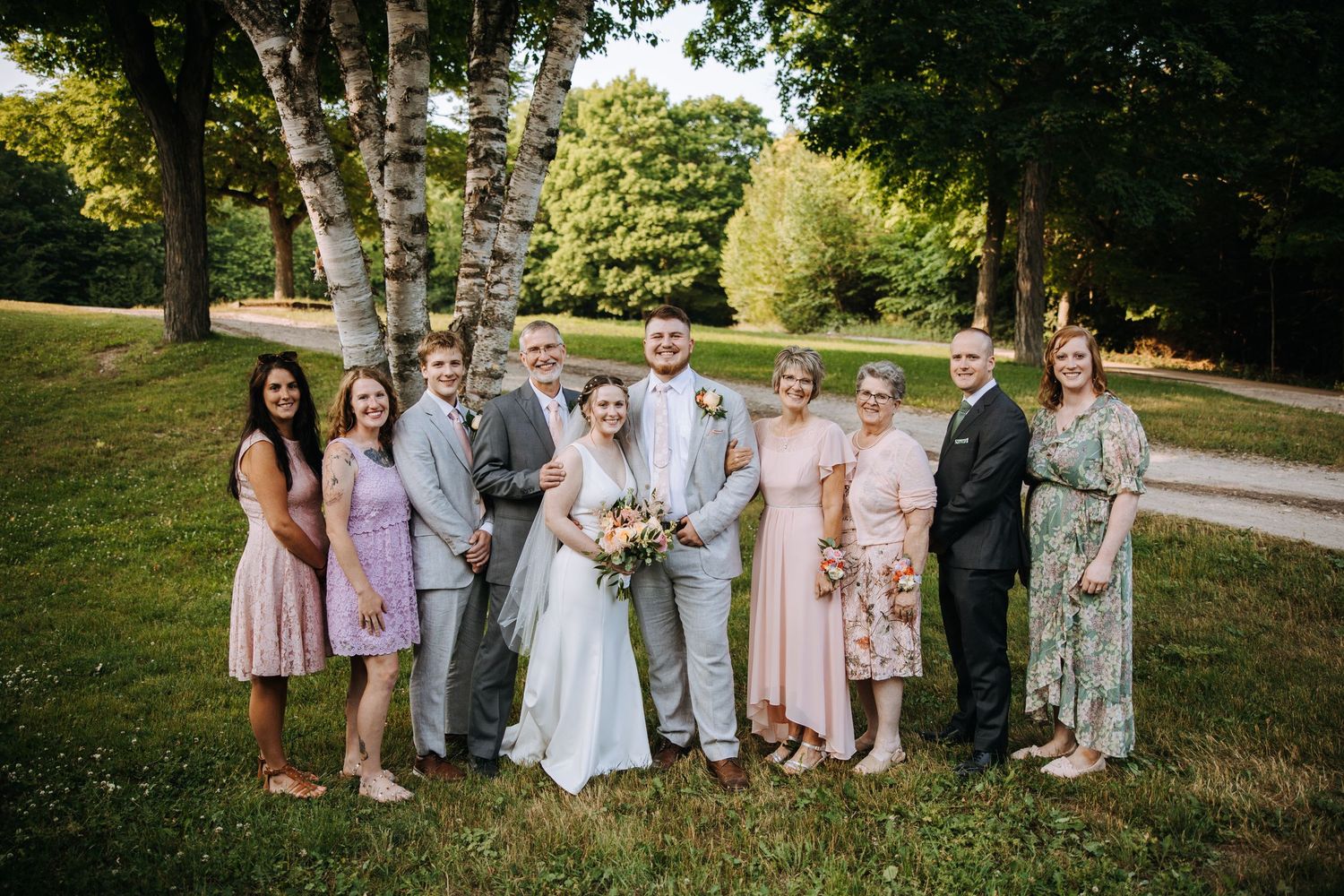 A wedding party poses together under birch trees on a sunny summer day.