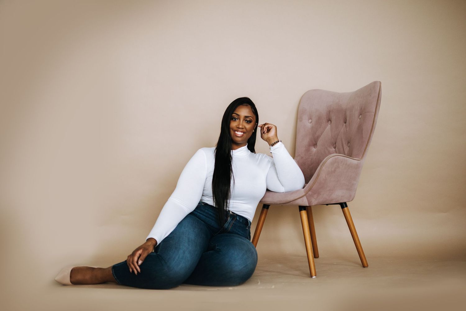 Studio portrait session with pink chair against neutral beige backdrop.