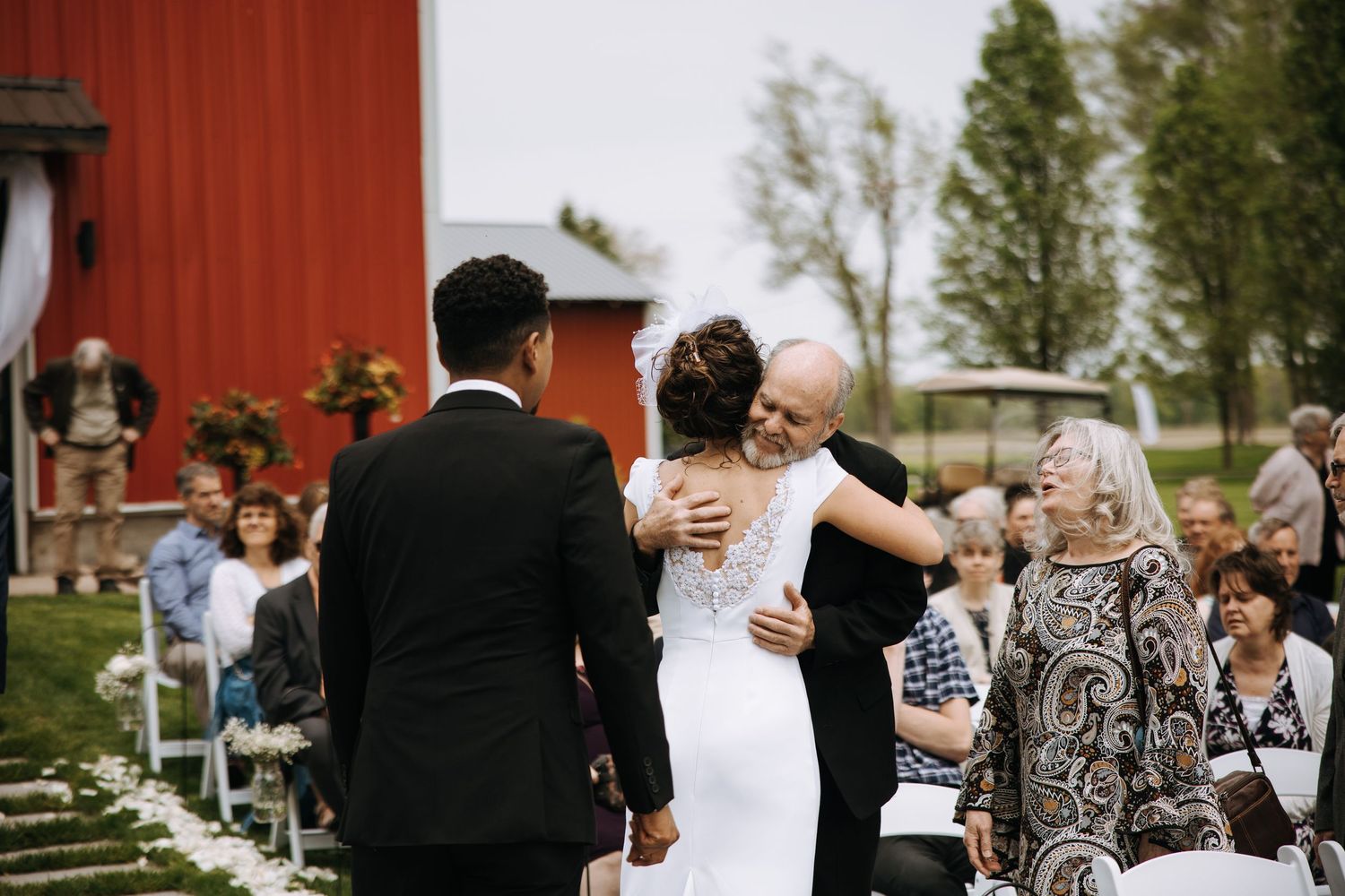 Wedding guests gather outside a red barn for outdoor celebration.