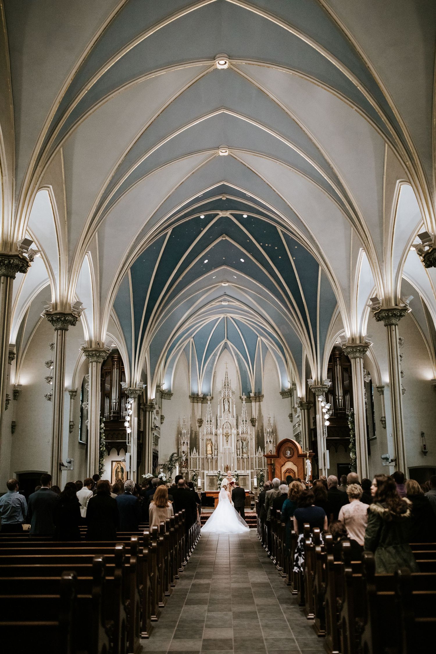 Gothic cathedral interior with vaulted ceilings and ornate arches illuminated by warm lighting during a wedding ceremony.