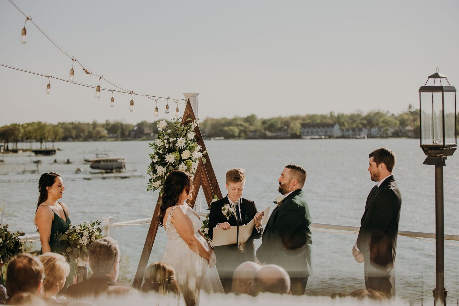 A lakeside wedding ceremony with string lights and floral arrangements at dusk.