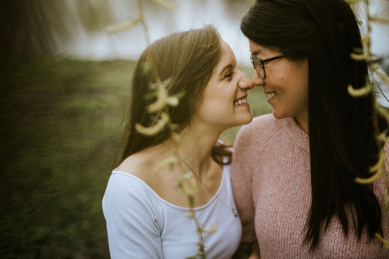 Two people share an intimate moment together outdoors while wearing casual clothing in soft natural lighting.