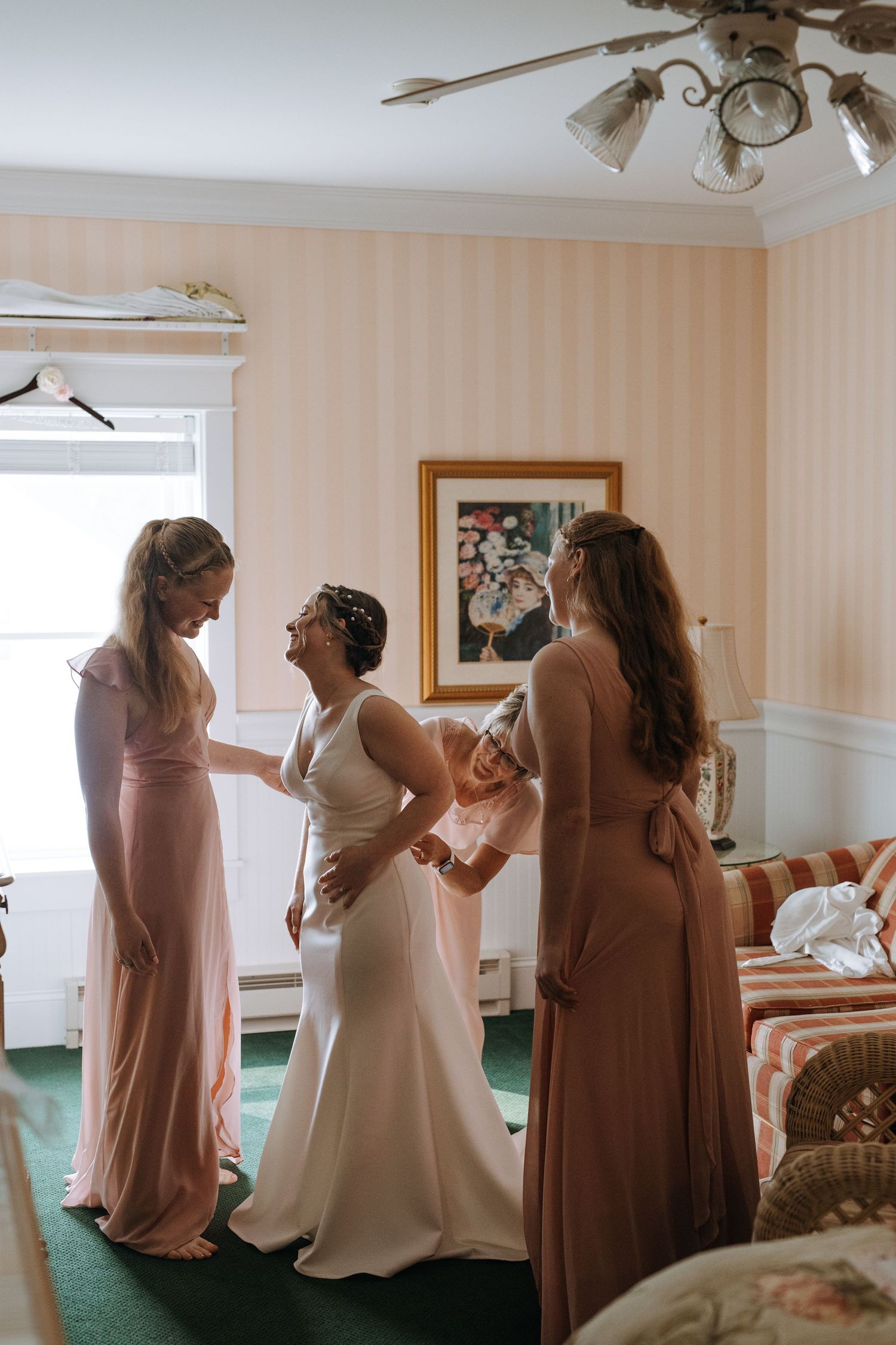 Bridesmaids help with wedding preparations in a room with green carpet and cream walls.