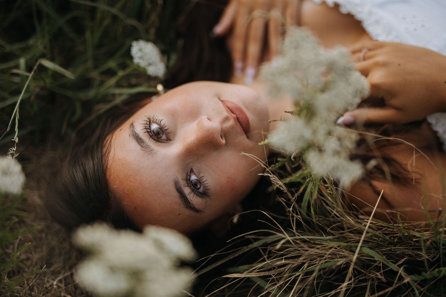 Artistic portrait lying in grass with white flowers in foreground.
