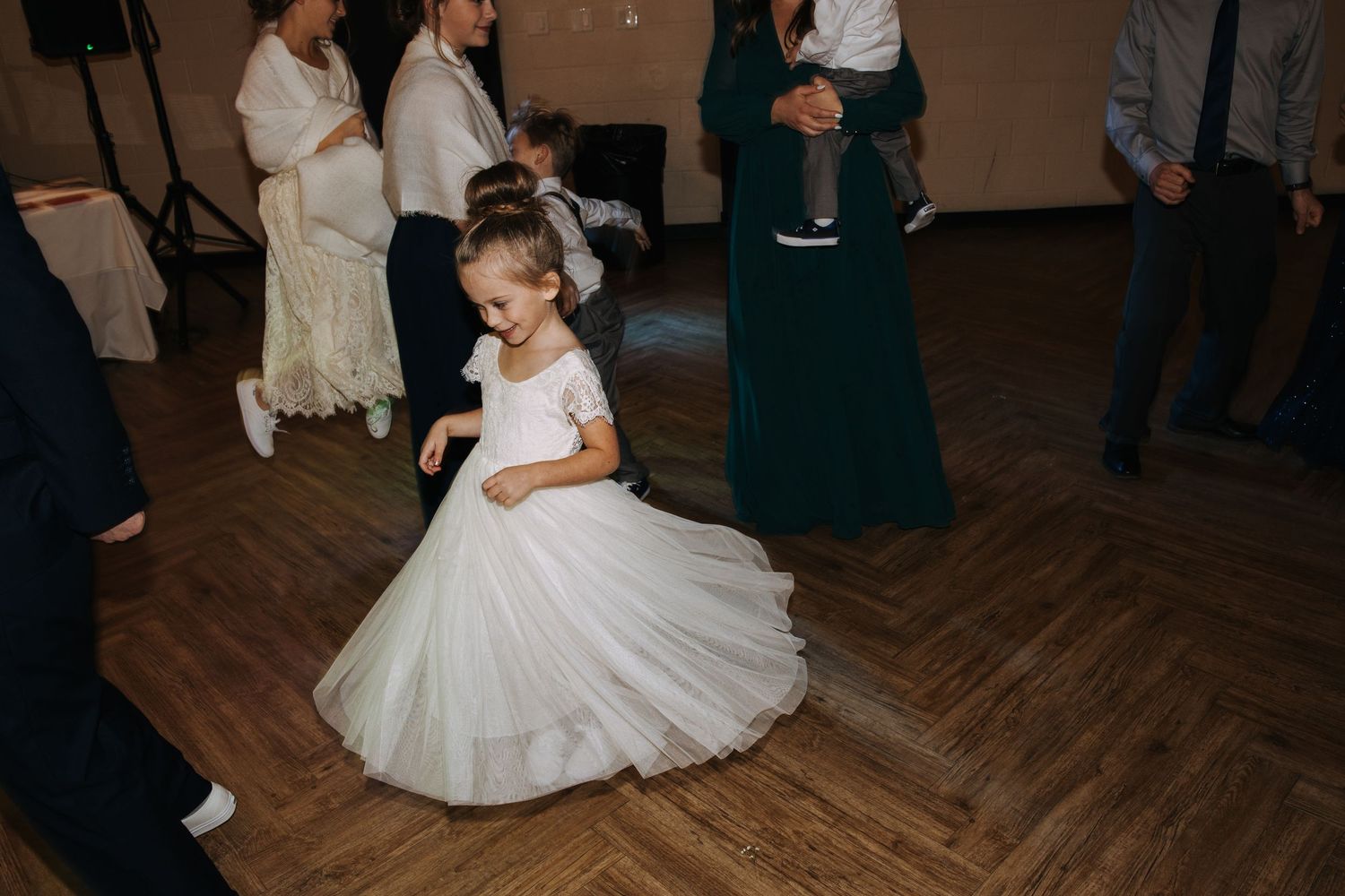 Wedding celebration on wooden dance floor with flowing white dresses in motion.