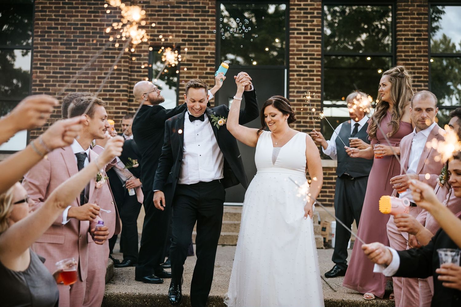 Wedding party celebrates outside brick building with confetti and champagne.