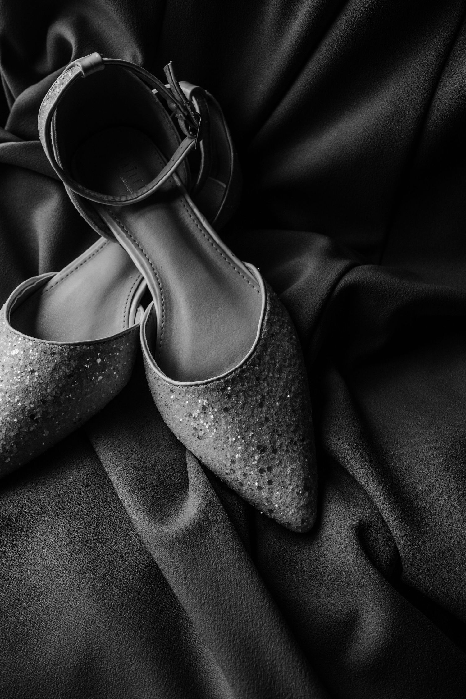 Close-up detail shot of sparkly bridal shoes on dark fabric with dramatic lighting.