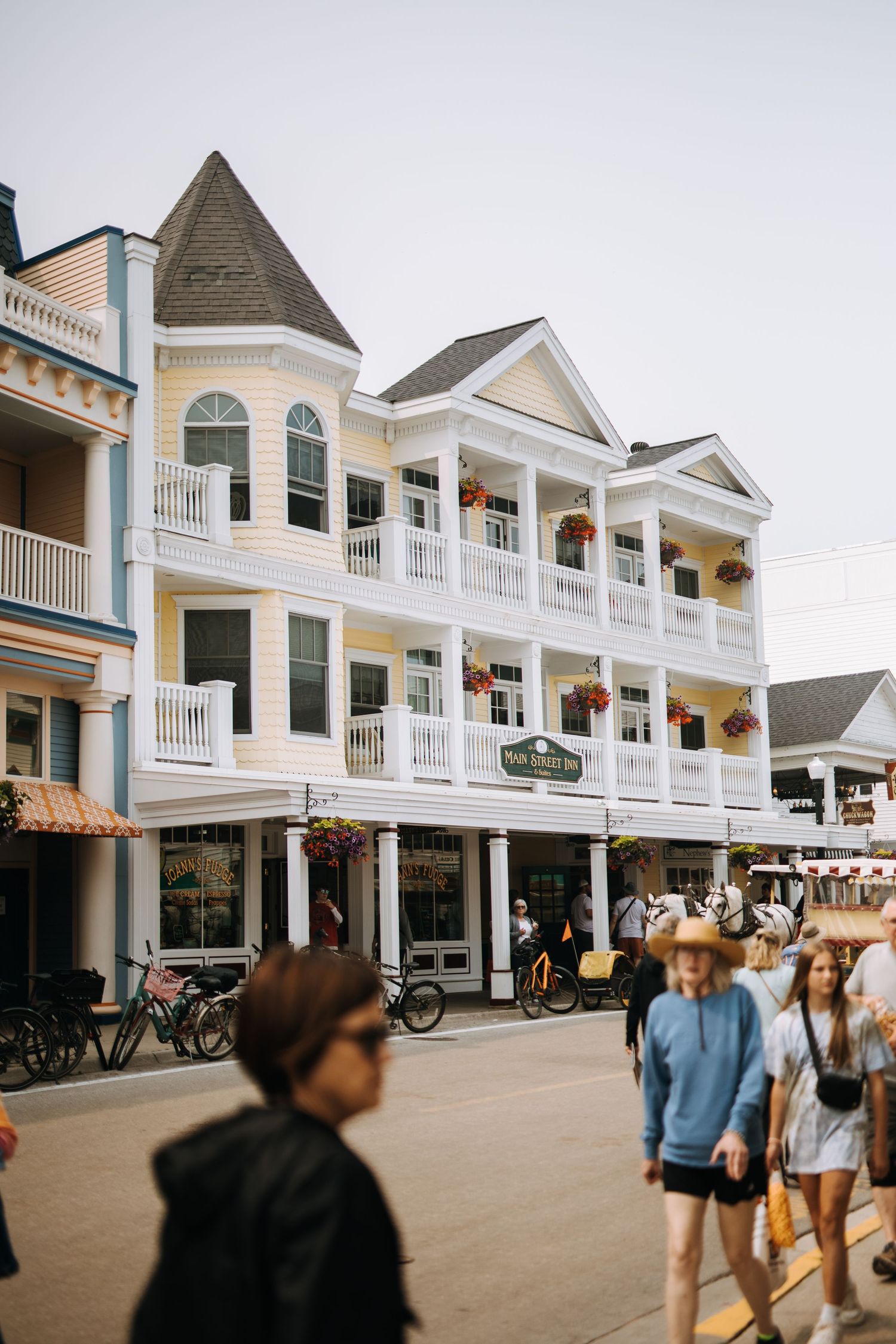 Historic Victorian-style buildings with white balconies line a bustling street on Mackinac Island.