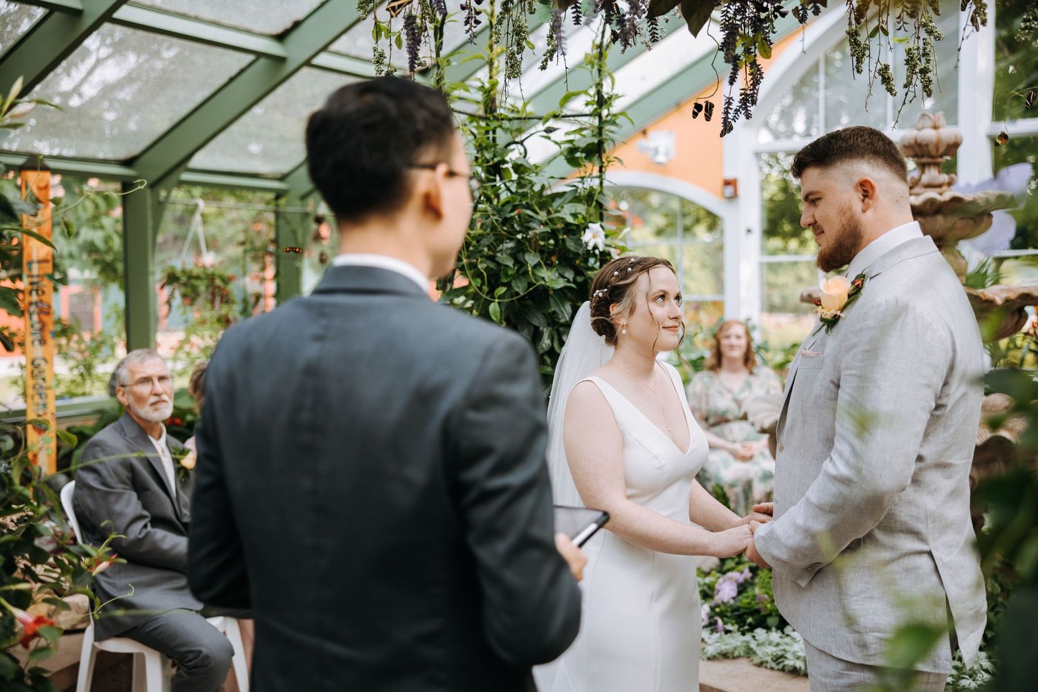 Wedding ceremony proceedings in a glass-enclosed garden setting.