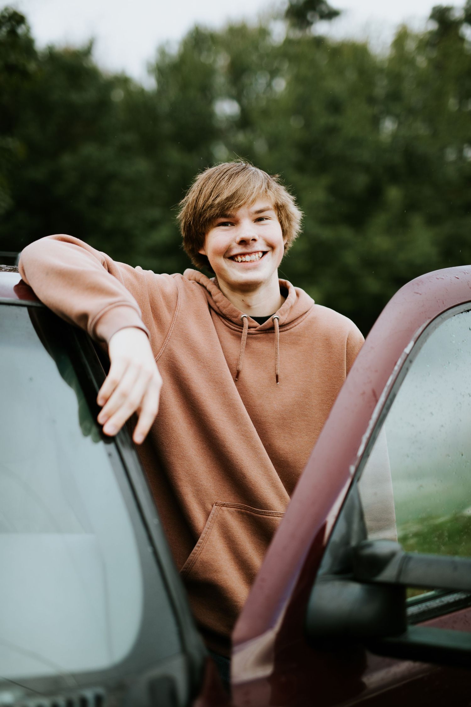 Person in brown hoodie leaning against car window during golden hour.