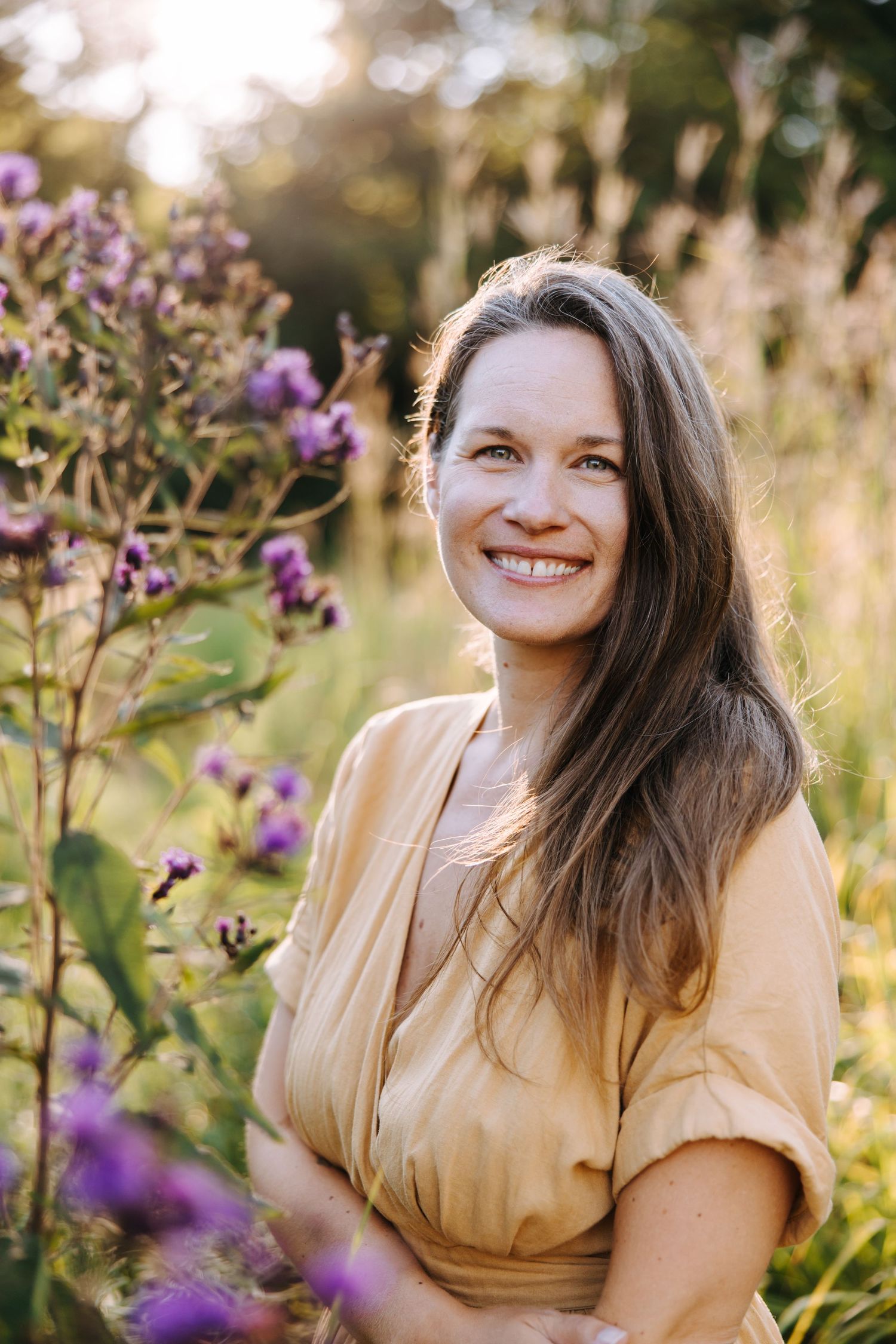 A person in a yellow top sits among blooming purple wildflowers in a sun-drenched meadow during golden hour.